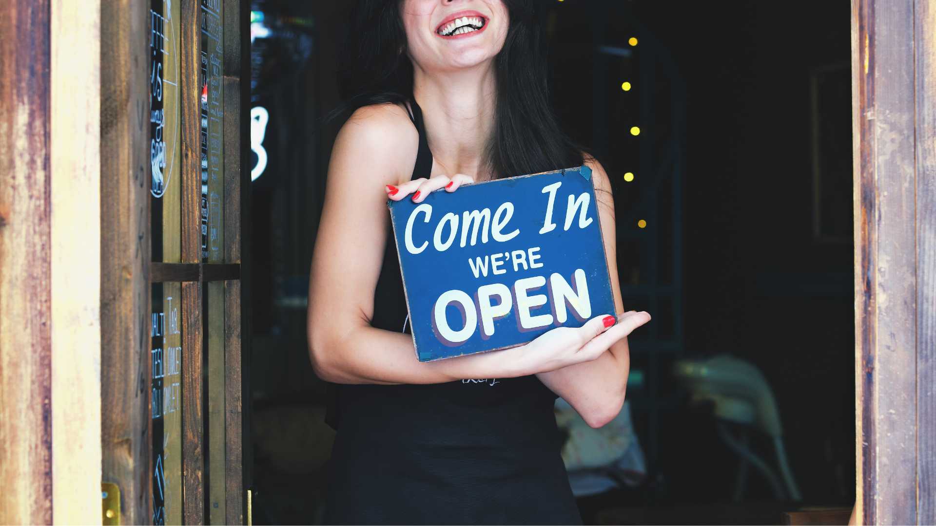 Femme tenant une pancarte où il est écrit " Come in, we are open"