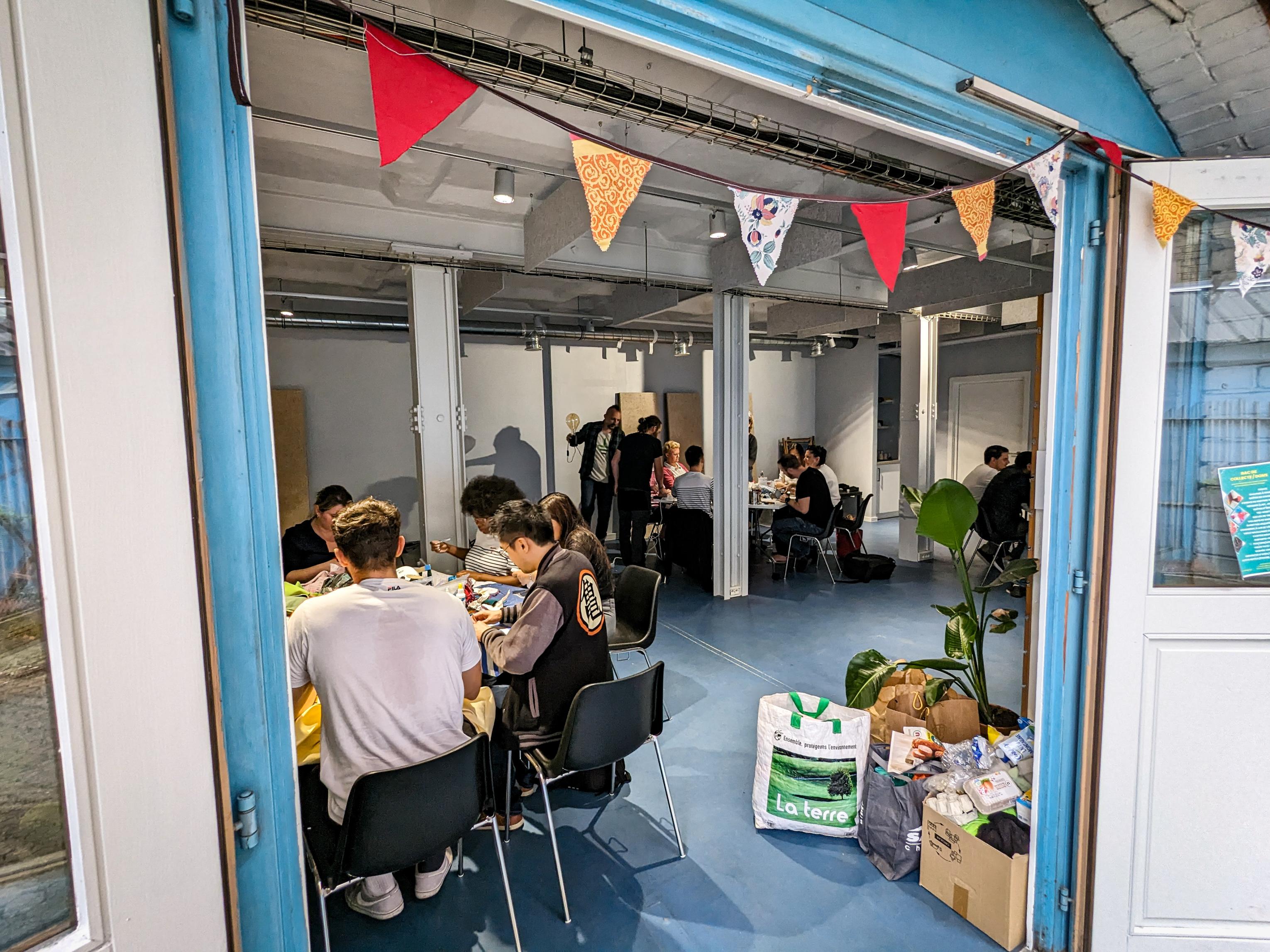 Photo d'un atelier dans les locaux de l'association. Une quinzaine de participant.e.s sont en train de bricoler avec des matériaux de récup'.